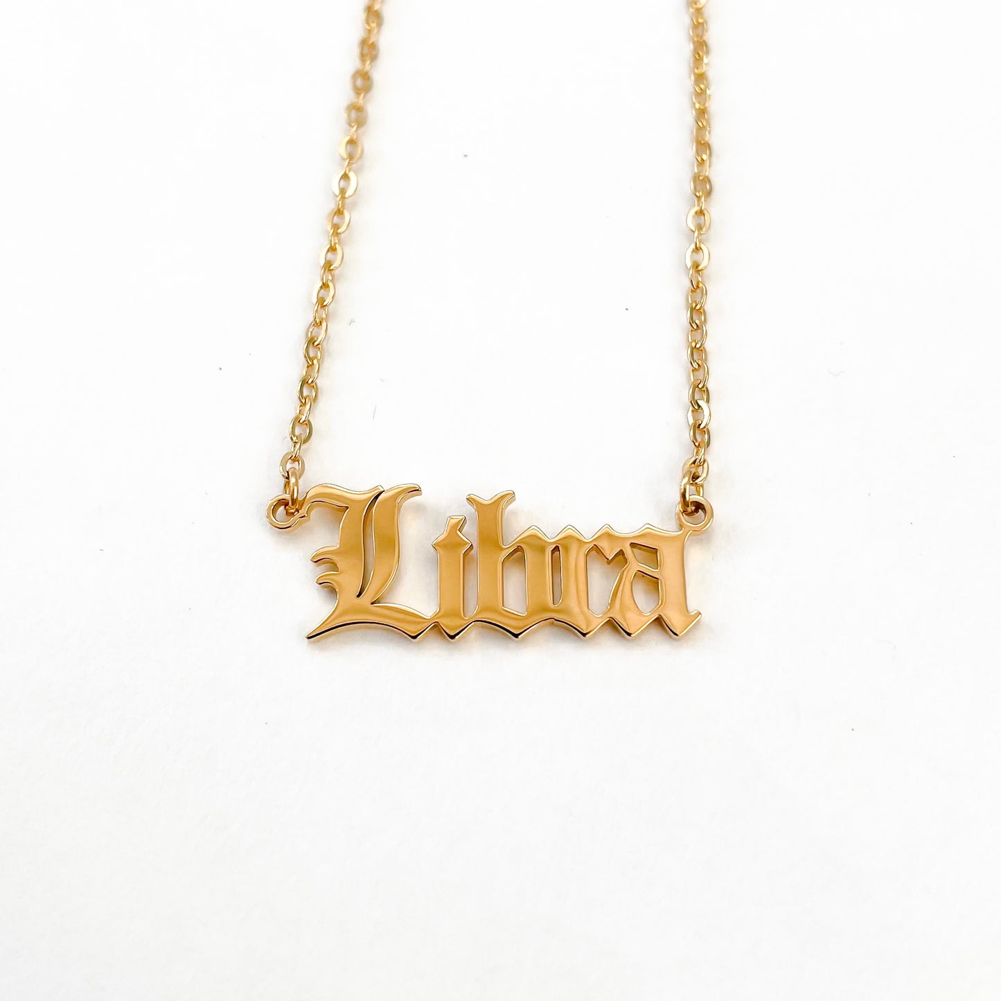 A gold-plated necklace with the word 'Libra' inscribed on a chain, displayed against a white background.