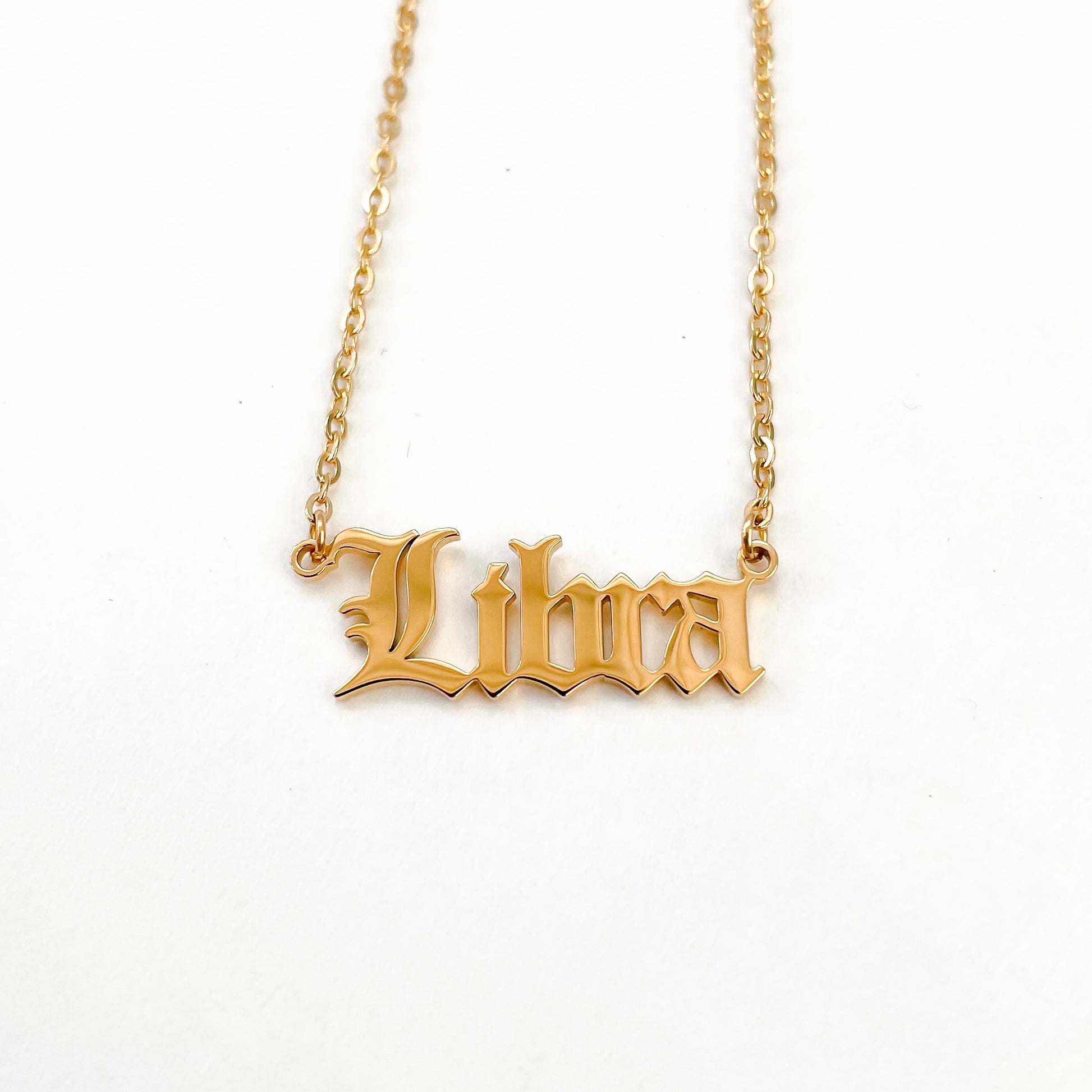 A gold-plated necklace with the word 'Libra' inscribed on a chain, displayed against a white background.
