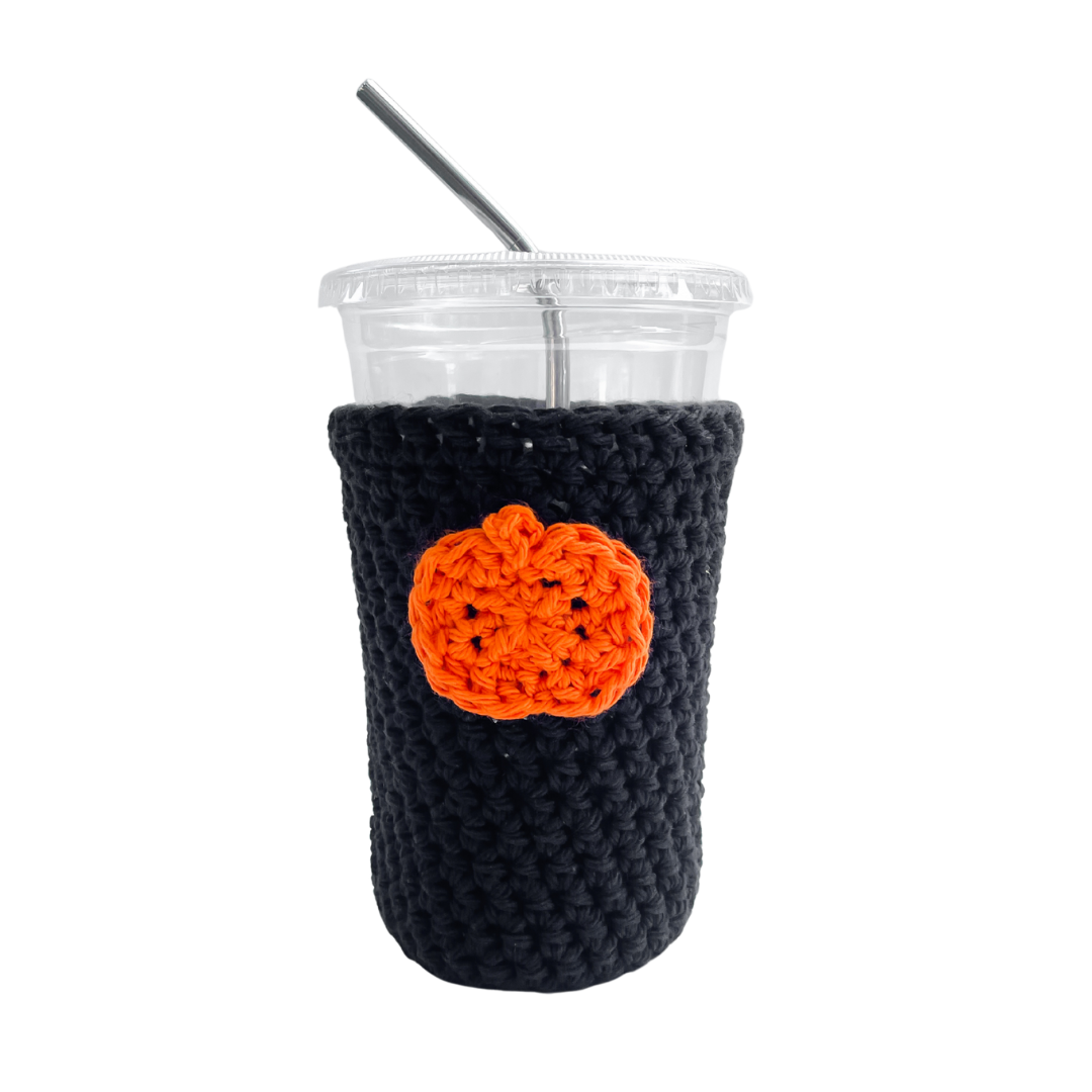 Black crocheted cup sleeve with an orange pumpkin design on a white background