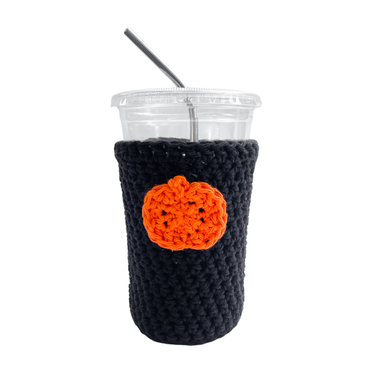 Black crocheted cup sleeve with an orange pumpkin design on a white background